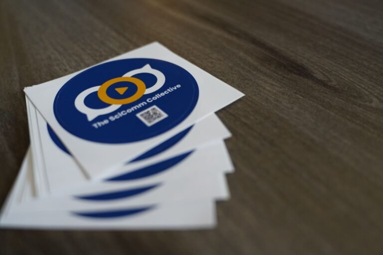 A stack of blue circle stickers with the Sci Comm Collective logo on them