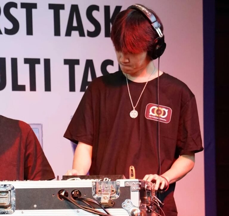 A tall Chinese man wearing headphones operating a DJ sound desk on a small stage