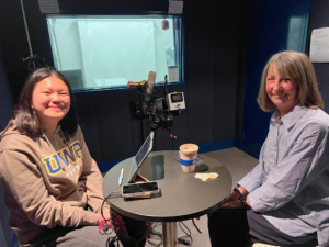 A smiling young woman in a UWA jumper and an older woman, also smiling, in an audio booth