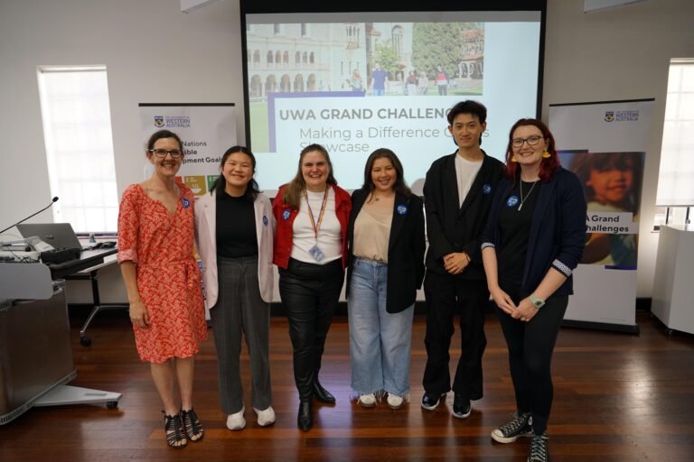 A group of people standing in front of a projector with UWA Grand Challenge on the presentation slide