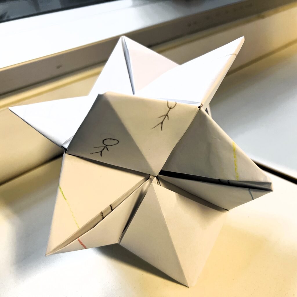 a 3D multi-pointed star made of white paper folded and fitted together. Drawings can be seen on some of the sides