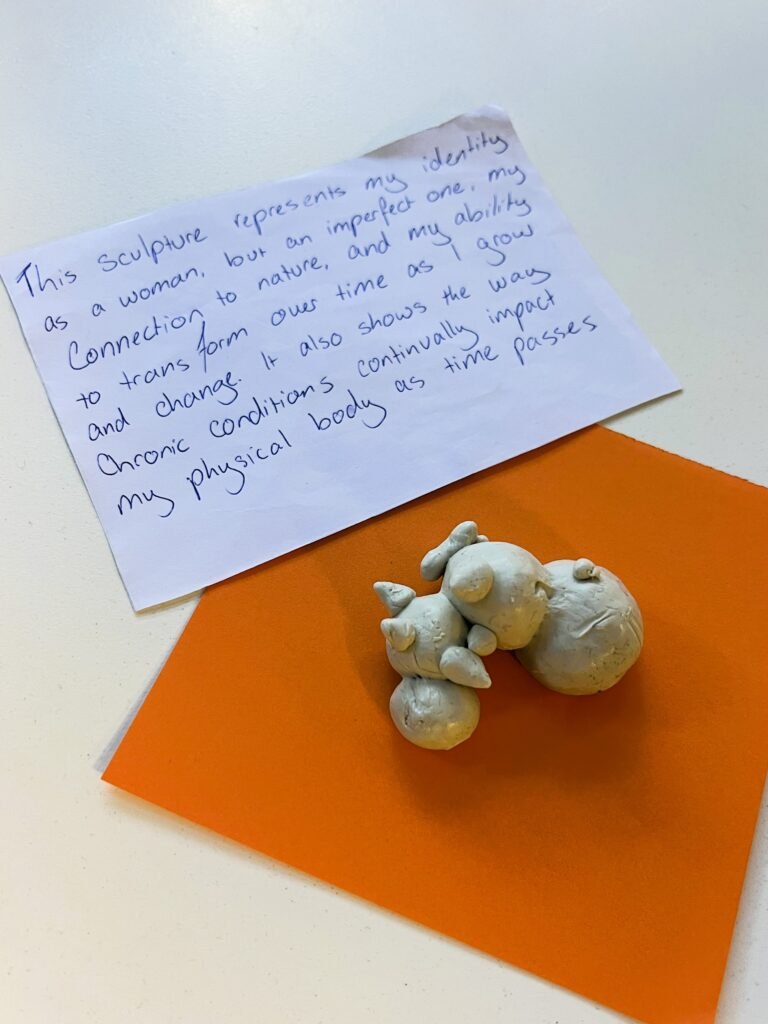 A clay caterpillar on a square of orange paper, with a reflection written on white paper next to it