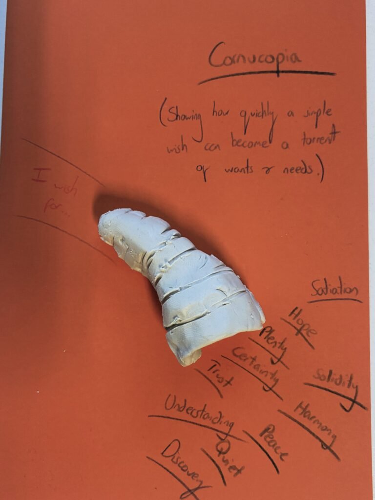 a white clay cornucopia on a piece of red-orange paper with words coming out of the cornucopia's mouth