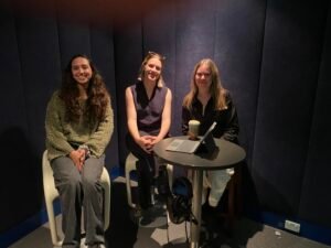 Three women sitting in a recording studio behind a round table with a laptop on it